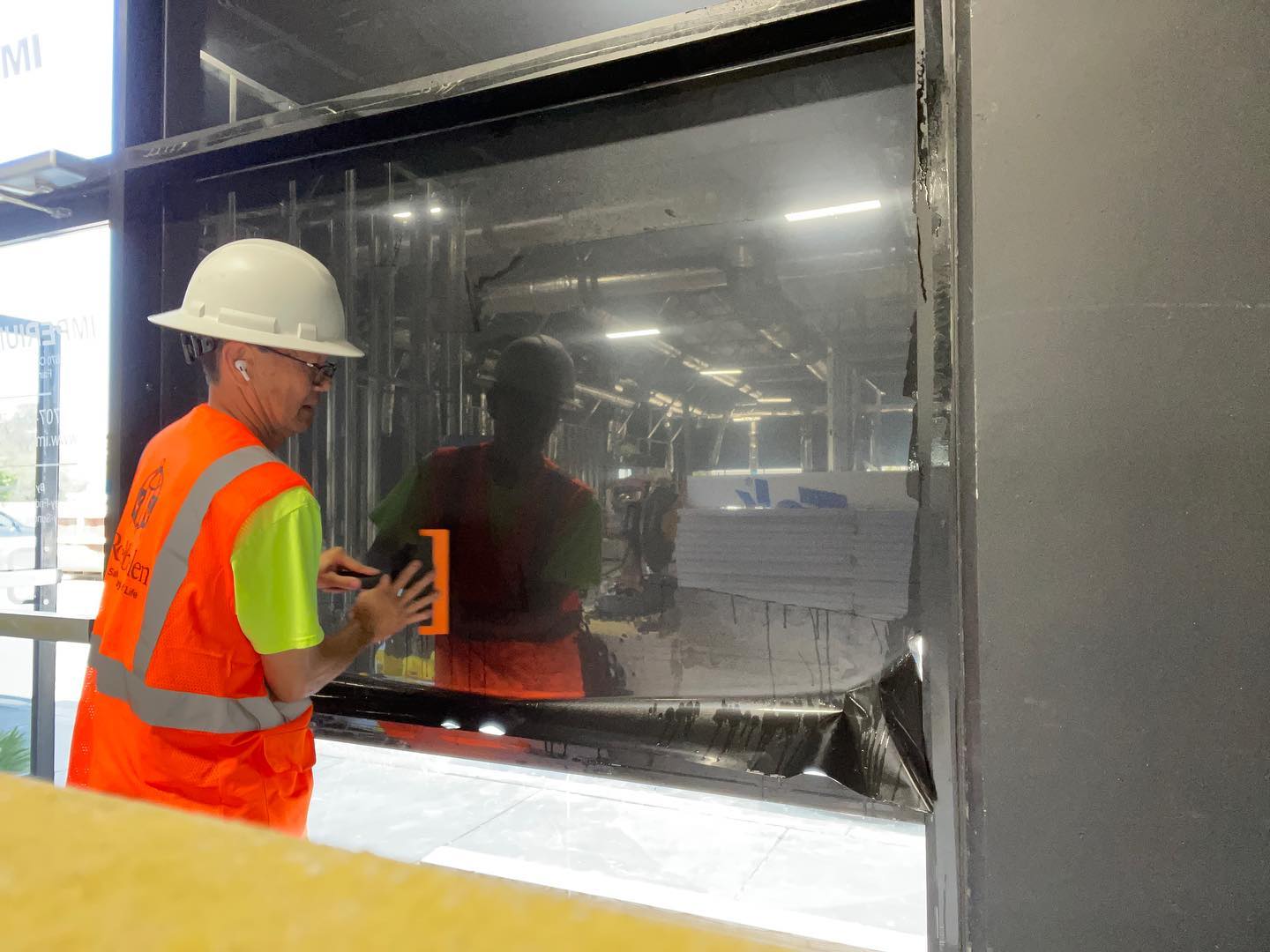 Installer in a hard hat and safety vest squeegeeing dark film onto a storefront window