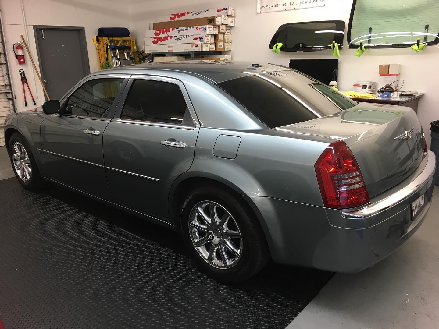 Chrysler 300 with freshly tinted windows parked inside the Pacific Window Tint shop, boxes of SunTek film on the rack behind it