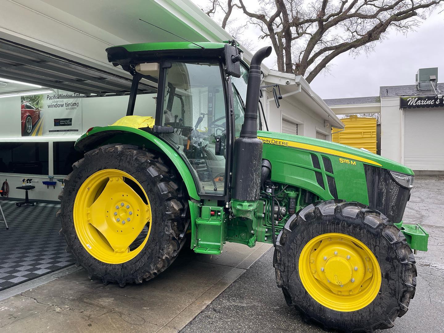 Green John Deere 5115M tractor parked outside the Pacific Window Tint bay